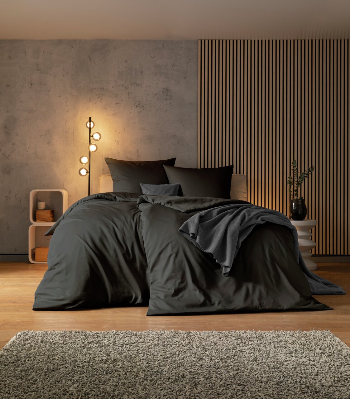 Schlafzimmer mit modernem Design, zeigt ein großes Bett mit dunkler Bettwäsche, umgeben von stilvoller Beleuchtung und Dekoration, aus frontaler Perspektive.