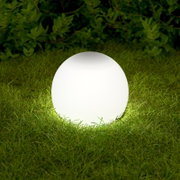 Leuchtende weiße Kugel-Gartenlampe auf Rasen vor grüner Hecke, frontale Ansicht auf Augenhöhe