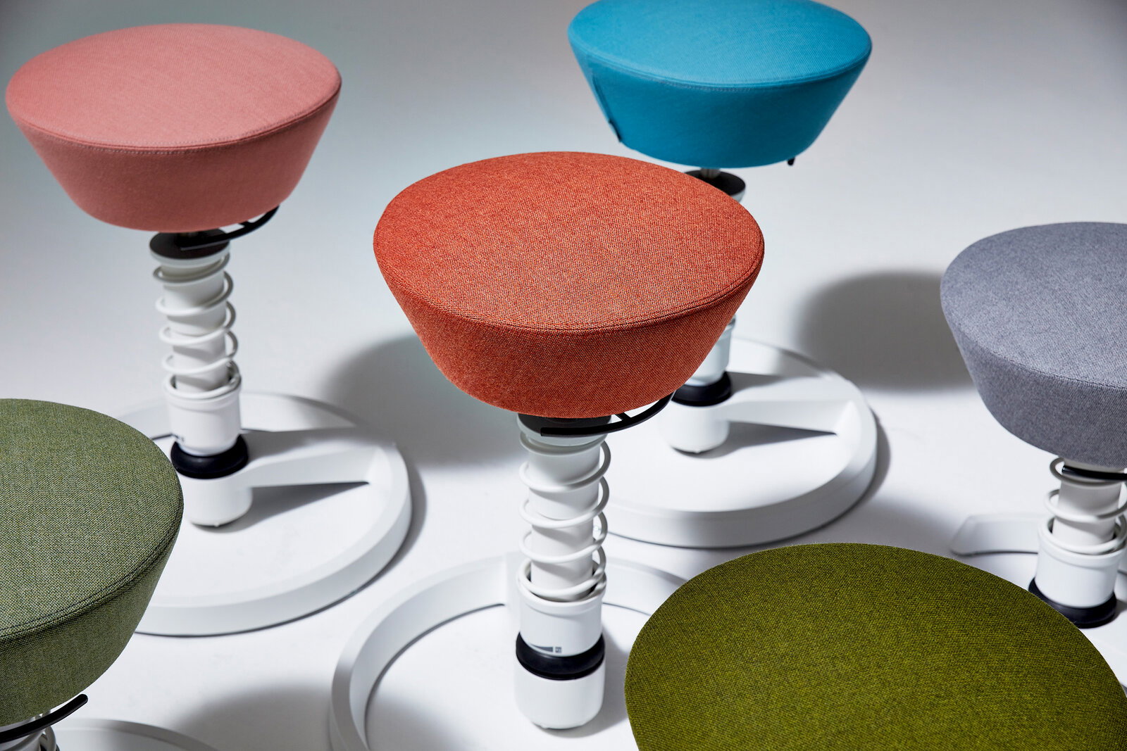 Verschiedene bunte Sitzhocker mit runden Sitzflächen und weißen Spiralfedern, aus der Vogelperspektive fotografiert.