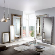 Mehrere große Spiegel mit dekorativen Rahmen in einem modernen Wohnzimmer, mit Blick auf eine helle Fensterfront.