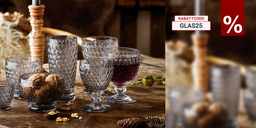 Rustikaler Holztisch mit dekorativen, facettierten Trinkgläsern, Nüssen und einer brennenden Kerze in gemütlicher Atmosphäre