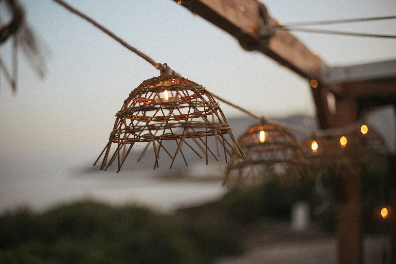 Nahaufnahme einer Outdoor-Lichterkette mit geflochtenen Lampenschirmen bei Sonnenuntergang