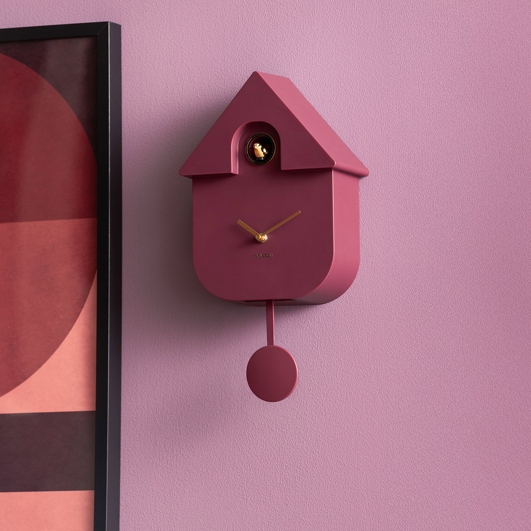 Moderne bordeauxfarbene Kuckucksuhr mit goldenen Zeigern an rosafarbener Wand, daneben Rabattcode GESCHENK25 für Geschenkartikel.