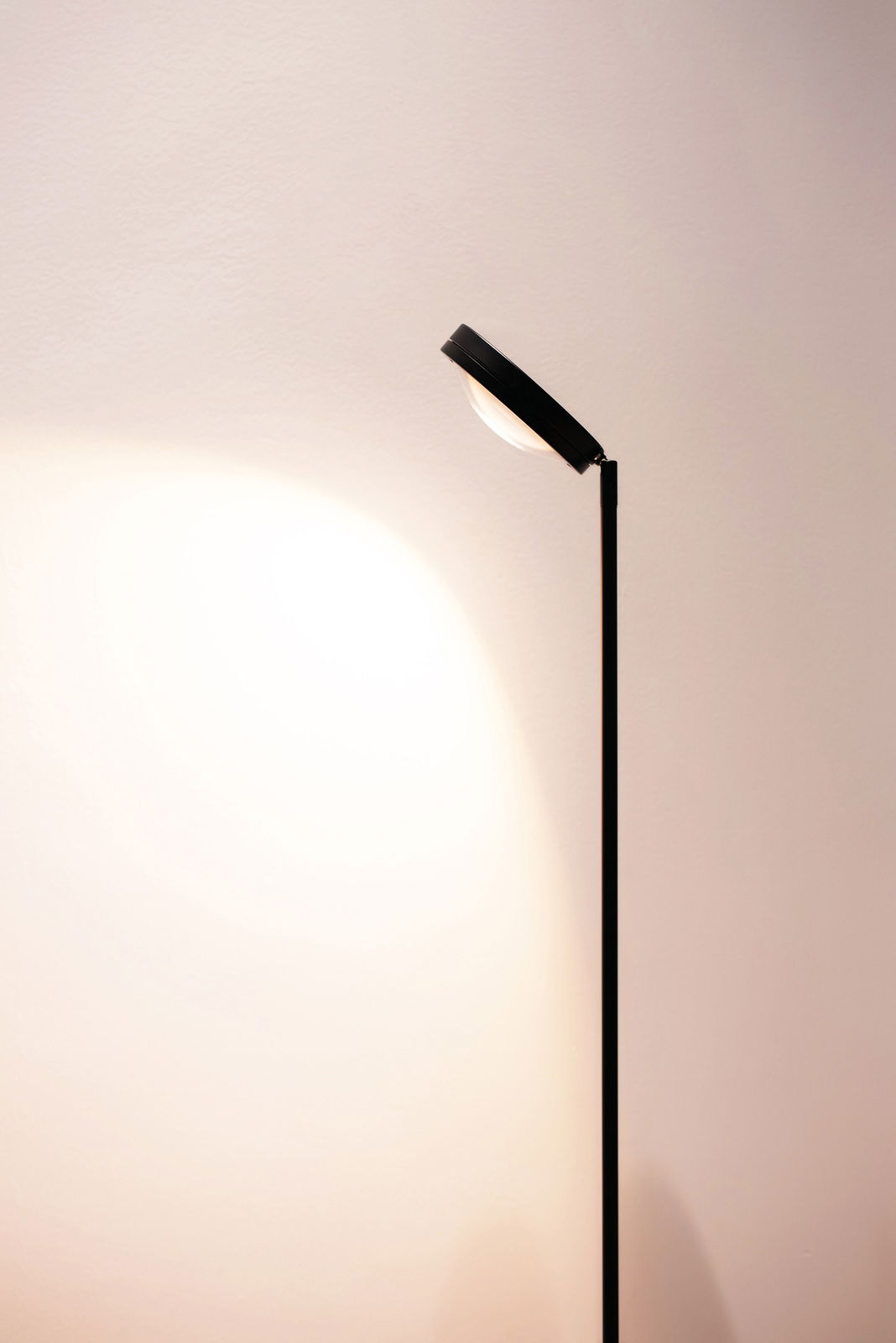 Schwarze LED Stehleuchte mit modernem Design, seitliche Perspektive, beleuchtet eine Wand.