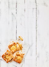 Draufsicht auf drei Stücke Apfelkuchen mit Mandelsplittern auf Backpapier, auf einem weißen Holztisch.
