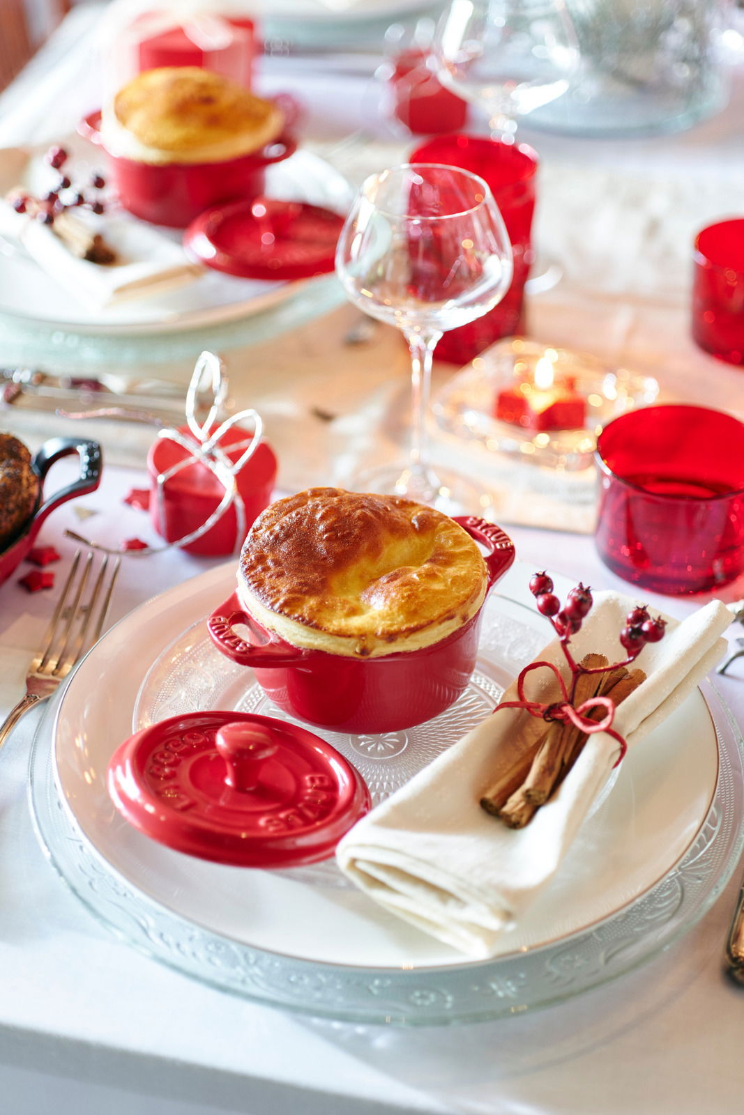 Rote Mini-Cocotte auf einem festlich gedeckten Tisch, von oben fotografiert, mit einem goldbraunen Auflauf und abgenommenem Deckel daneben.