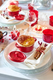 Rote Mini-Cocotte auf einem festlich gedeckten Tisch, von oben fotografiert, mit einem goldbraunen Auflauf und abgenommenem Deckel daneben.