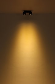 Zweiflammiger LED Strahler an der Decke, der warmes Licht auf die Wand wirft, aus der Perspektive von unten betrachtet.