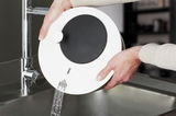 Salatschleuder ROTARE in der Anwendung, Wasser wird aus der Schleuder in ein Spülbecken abgegossen, seitliche Perspektive