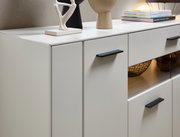 Nahaufnahme eines modernen weißen Sideboards mit schwarzen Griffen, dekoriert mit Skulpturen und Büchern, seitliche Perspektive.