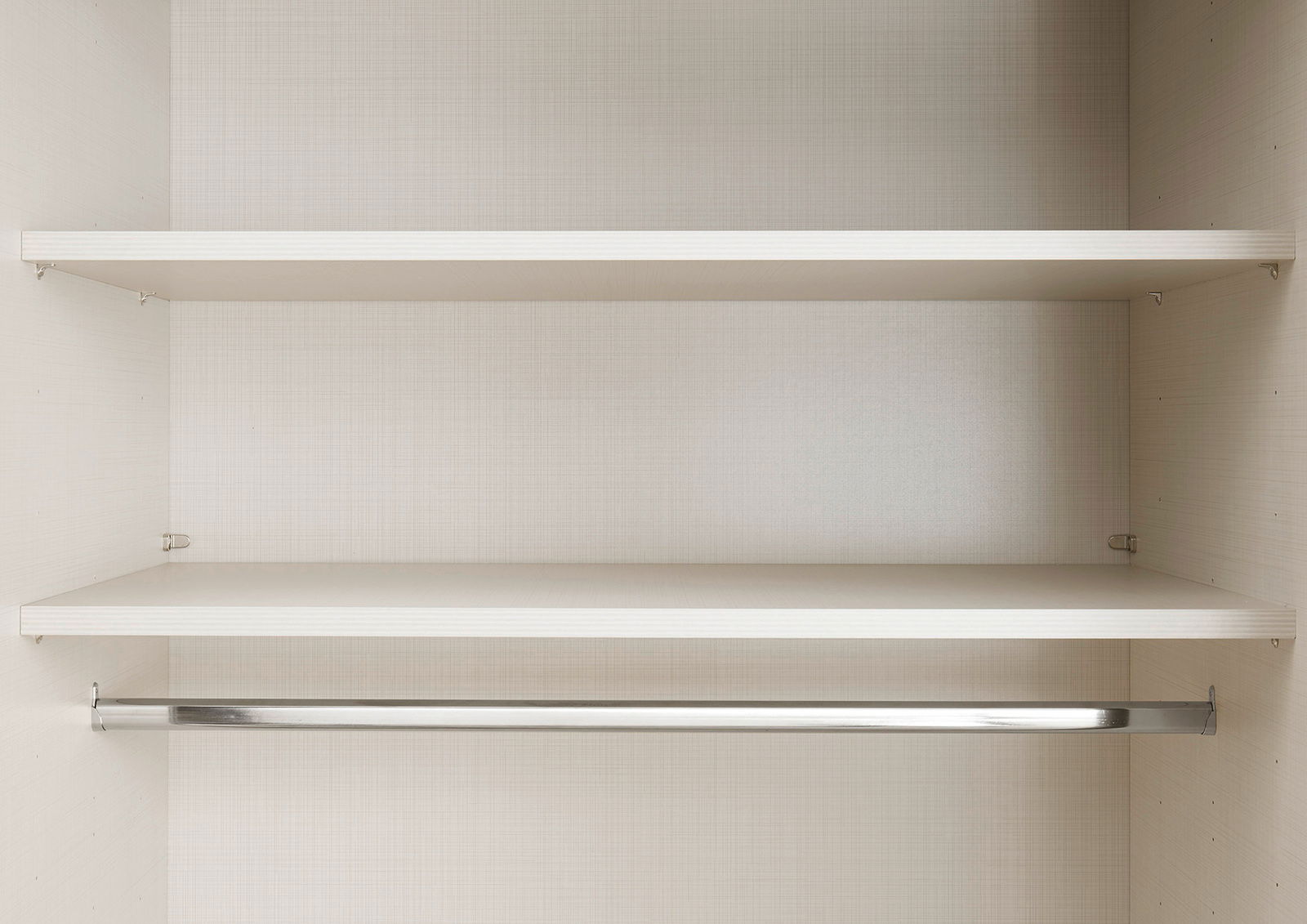 Innenansicht eines Schwebetürenschranks mit zwei Einlegeböden und einer Kleiderstange, frontal betrachtet.