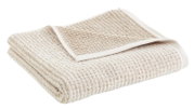 Een beige handdoek met een gestructureerd oppervlak, opgevouwen en gefotografeerd vanuit een zijaanzicht.