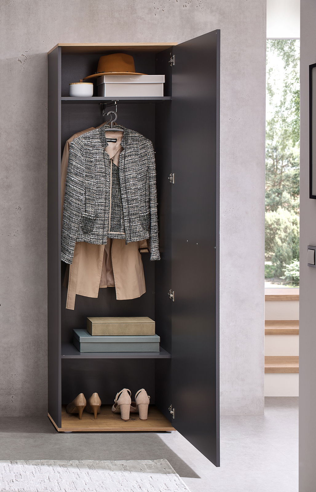 Geöffneter Hochschrank in moderner Umgebung, gefüllt mit Kleidung, Schuhen und Aufbewahrungsboxen, frontal betrachtet.