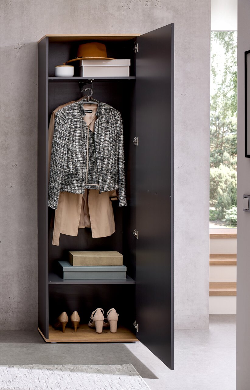 Geöffneter Hochschrank in moderner Umgebung, gefüllt mit Kleidung, Schuhen und Aufbewahrungsboxen, frontal betrachtet.