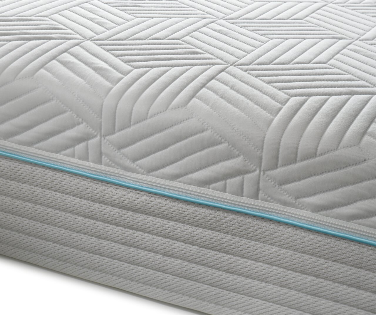 Nahaufnahme einer Gel-Kaltschaummatratze mit geometrischem Muster und blauer Ziernaht, seitliche Perspektive.