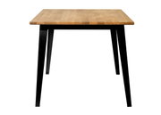 Moderne eettafel met houten blad en zwarte metalen poten, van voren gefotografeerd.