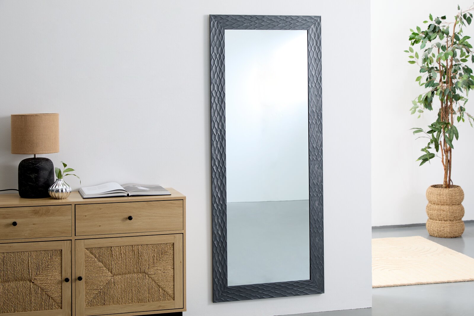 Großer rechteckiger Spiegel mit dekorativem Rahmen, an einer Wand lehnend. Perspektive von vorne.