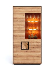 Hoher Holzschrank/Vitrine in Eichenoptik mit beleuchtetem Glas-Regalfach und Gläsern, frontale Ansicht.