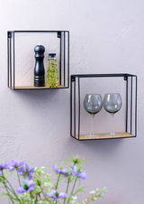 Zwei Wandregale aus Metall mit Holzablage, eines mit Gewürzmühle und Ölflasche, das andere mit zwei Weingläsern, seitliche Perspektive.