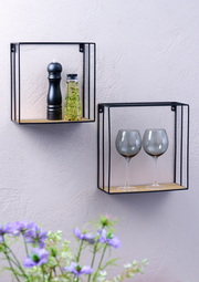 Zwei Wandregale aus Metall mit Holzablage, eines mit Gewürzmühle und Ölflasche, das andere mit zwei Weingläsern, seitliche Perspektive.
