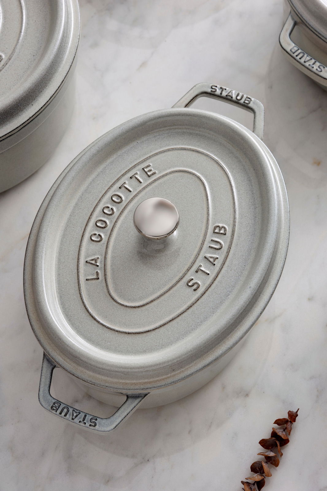 Ovale Cocotte aus Gusseisen in Grau mit Deckel, von oben fotografiert, auf einer Marmoroberfläche.