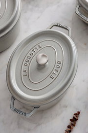 Ovale Cocotte aus Gusseisen in Grau mit Deckel, von oben fotografiert, auf einer Marmoroberfläche.