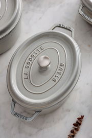 Ovale Cocotte aus Gusseisen in Grau mit Deckel, von oben fotografiert, auf einer Marmoroberfläche.