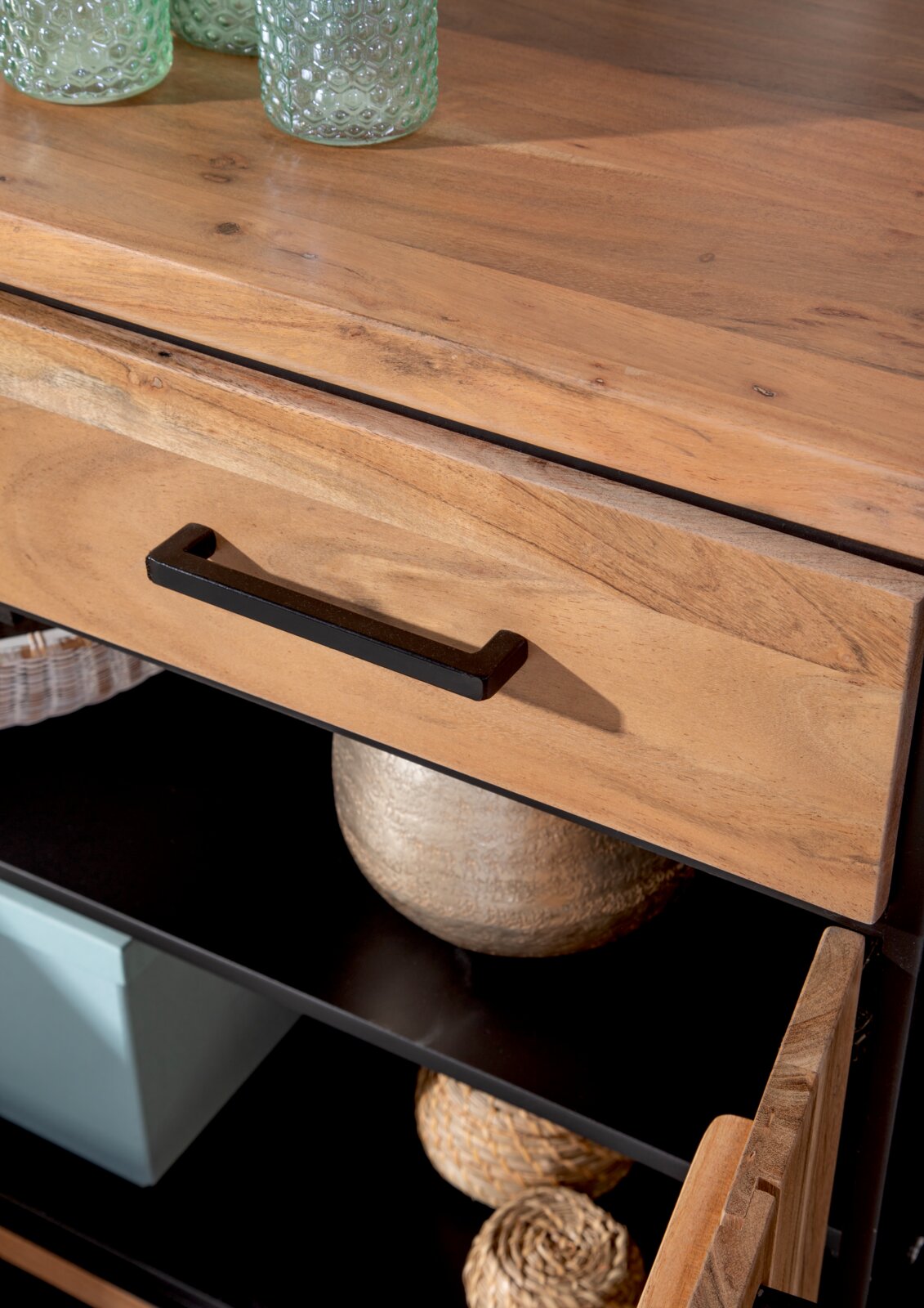 Close-up van een houten dressoir met een zwarte handgreep, een gedeeltelijk geopende lade en planken met decoraties, gezien vanuit vogelperspectief.