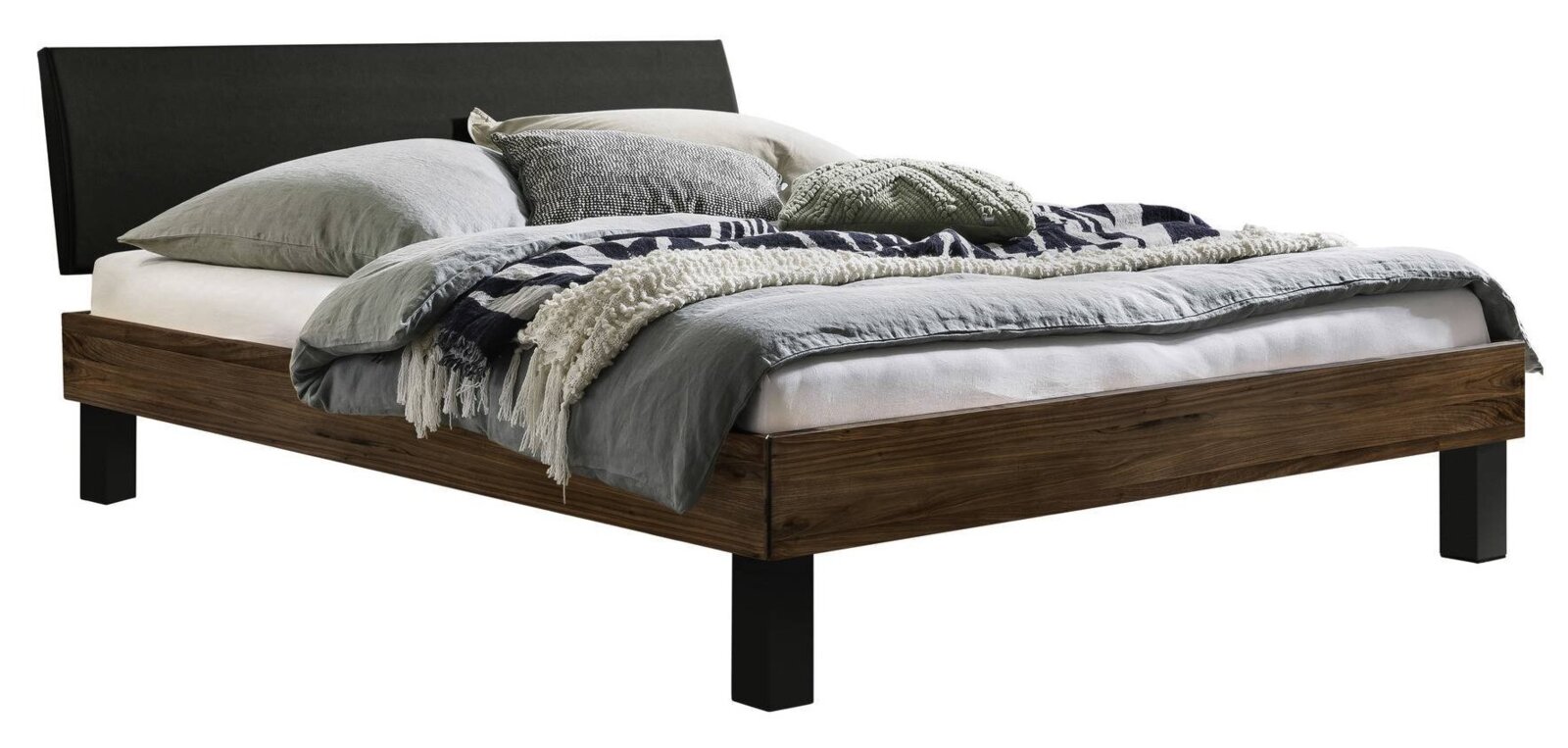 Modern tweepersoonsbed met houten frame in donkere eikenlook, zwart gestoffeerd hoofdeinde en zwarte poten, met grijs beddengoed en kussens, schuin van linksvoor gefotografeerd.