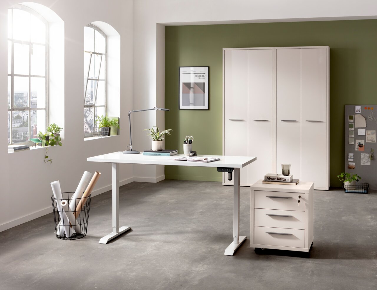 E-Serie Tischplatte E-START Moderner, elektrisch höhenverstellbarer Schreibtisch in einem hellen Büro mit grüner Akzentwand, seitlicher Perspektive.
