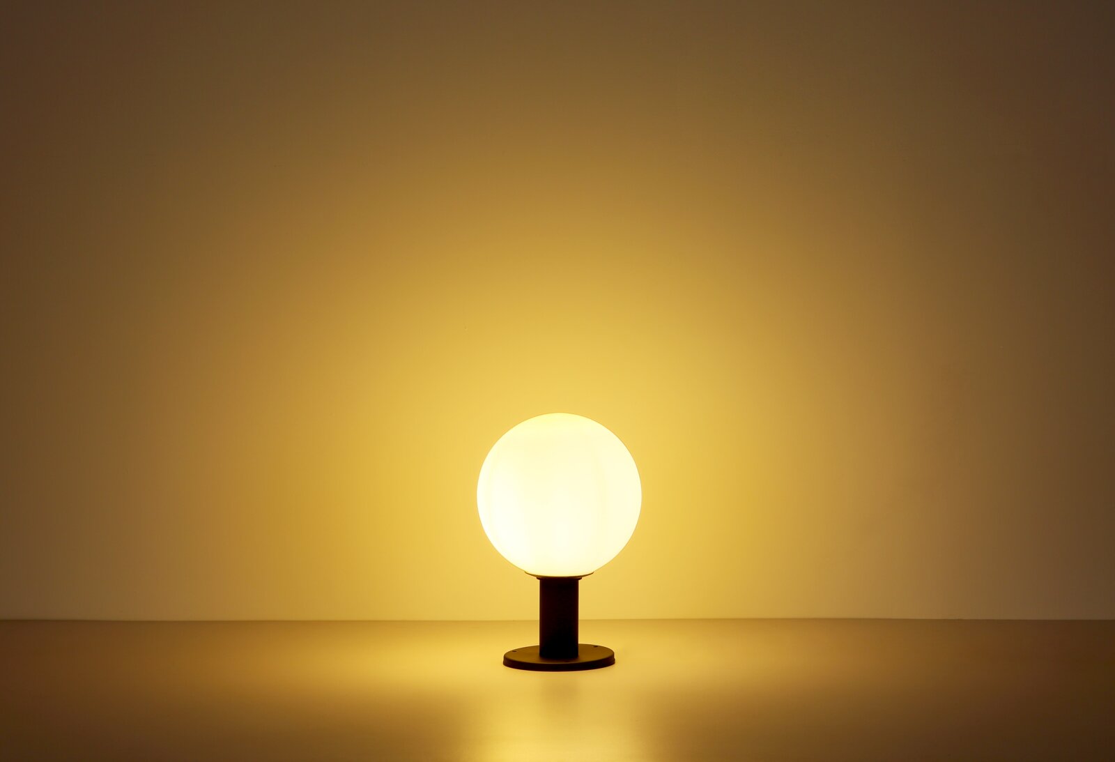 Kugelförmige Außenleuchte auf einem Tisch, frontal beleuchtet mit warmem Licht