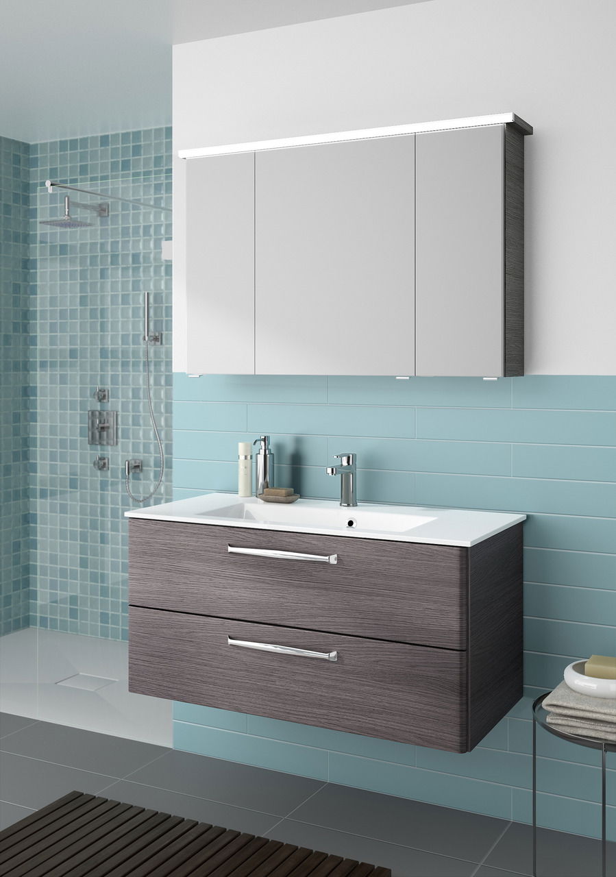 Moderner Badblock mit grauen Schubladen und weißem Waschbecken, frontal betrachtet, vor einer Wand mit blauen Fliesen.