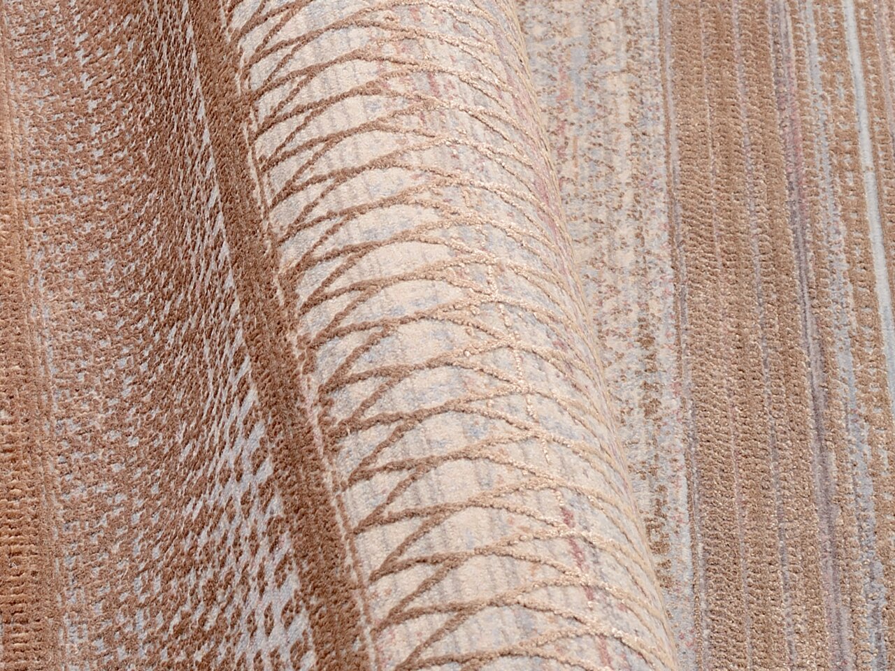 Nahaufnahme eines Designer Teppichs mit geometrischem Muster in Beige- und Brauntönen, aus seitlicher Perspektive aufgenommen.