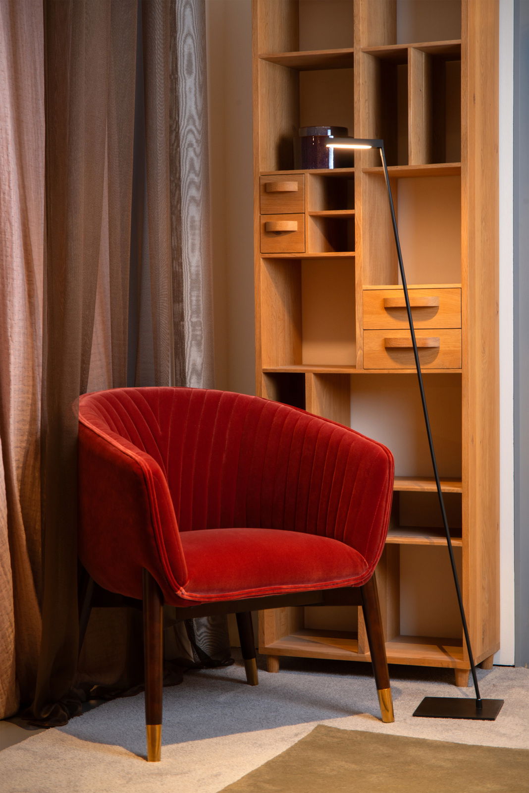 Steh- und Leseleuchte Lucide LAVALE in einem gemütlichen Wohnzimmer, neben einem roten Sessel und einem Holzregal, aus seitlicher Perspektive.