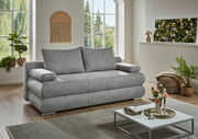 Graues Funktionssofa in einem modernen Wohnzimmer mit großen Fenstern und Pflanzen, seitliche Perspektive.