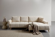Modernes beiges Ecksofa mit Chaise longue rechts, gestepptem Sitz und Holzfüßen, frontal aus leicht erhöhter Perspektive im minimalistischen Wohnzimmer mit Beistelltisch, Kissen und Decke.