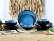 Tellerset 18-tlg mit blauer Innenseite und schwarzer Außenseite, frontal präsentiert auf einem Holztisch mit dekorativen Elementen.