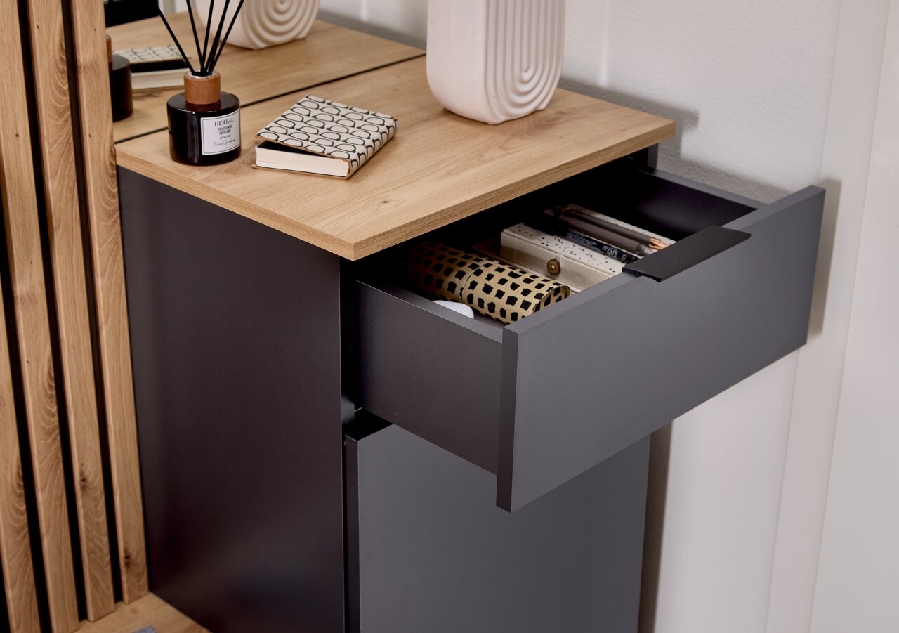 Nahaufnahme einer Kompaktgarderobe mit Holzoberfläche und geöffneter Schublade, die verschiedene Gegenstände enthält. Perspektive von schräg oben.