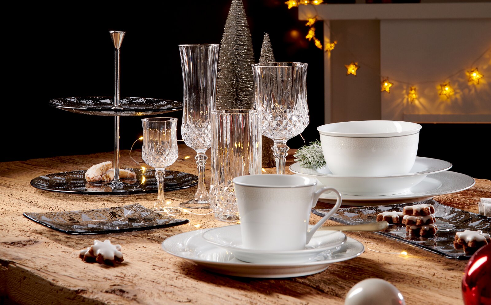 Festlich gedeckter Weihnachtstisch mit weißem Porzellan, eleganten Kristallgläsern und schwarzer Etagere, aus leicht erhöhter Frontperspektive inszeniert