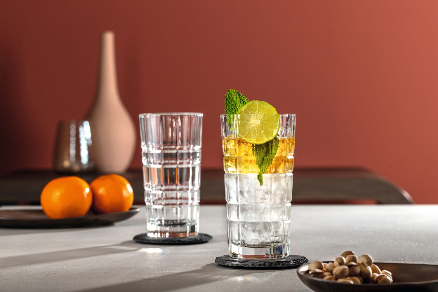 Zwei Longdrinkgläser SPIRITII 400ml auf einem Tisch, eines gefüllt mit einem Getränk, Eis, Limettenscheibe und Minze, aus seitlicher Perspektive fotografiert.