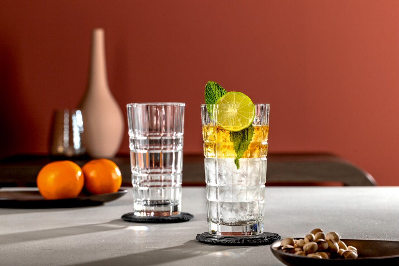 Zwei Longdrinkgläser SPIRITII 400ml auf einem Tisch, eines gefüllt mit einem Getränk, Eis, Limettenscheibe und Minze, aus seitlicher Perspektive fotografiert.