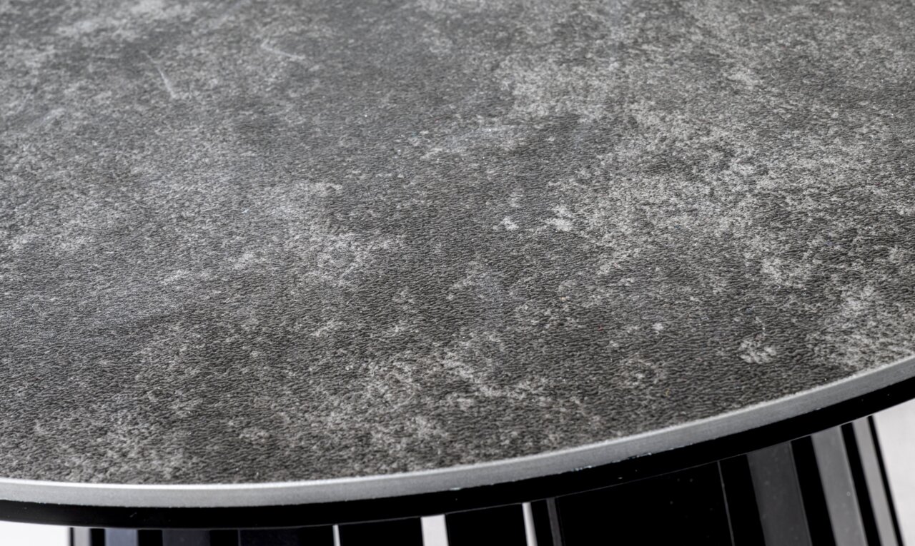Nahaufnahme eines Couchtischs mit grauer, strukturierter Oberfläche und schwarzem Gestell, von oben betrachtet.