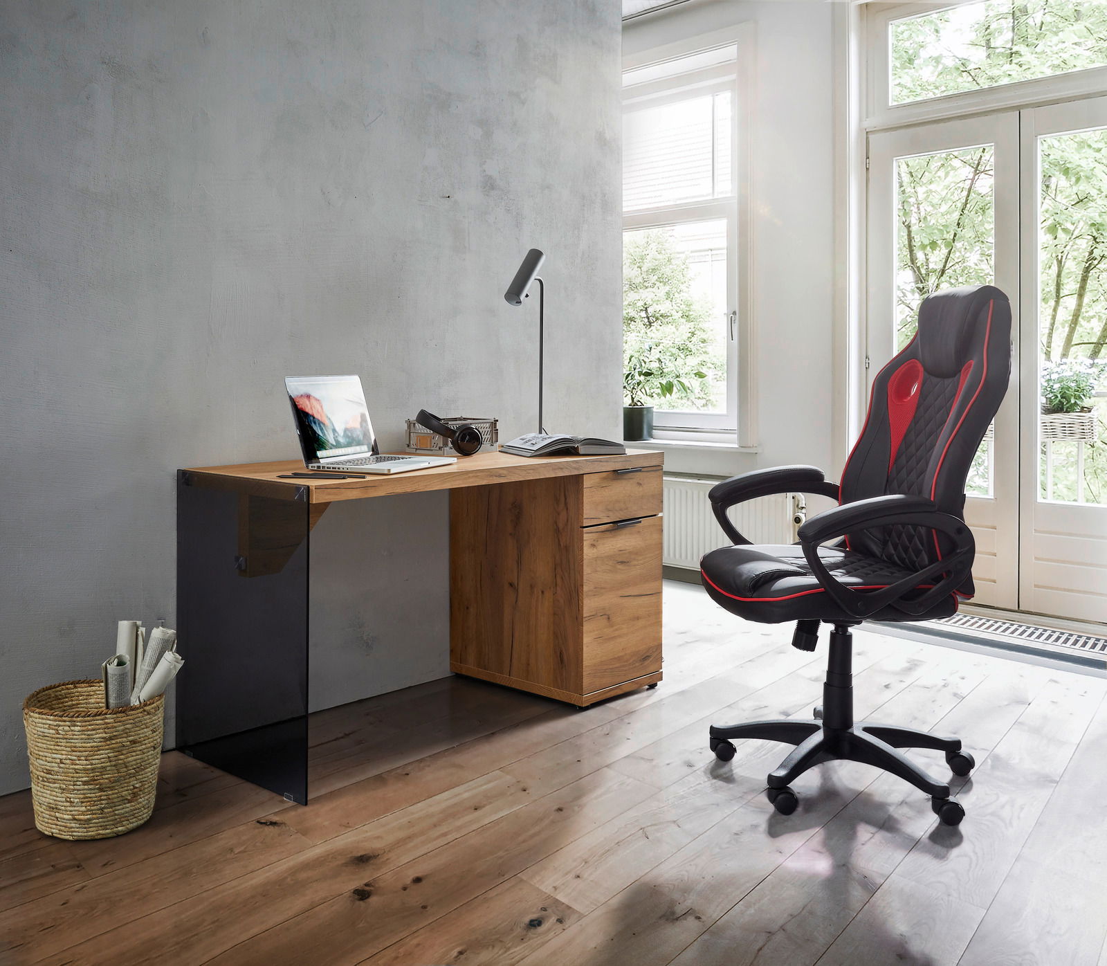 Moderner Gaming-Stuhl in Schwarz und Rot, seitliche Perspektive, neben einem Schreibtisch in einem hellen Raum mit großen Fenstern.