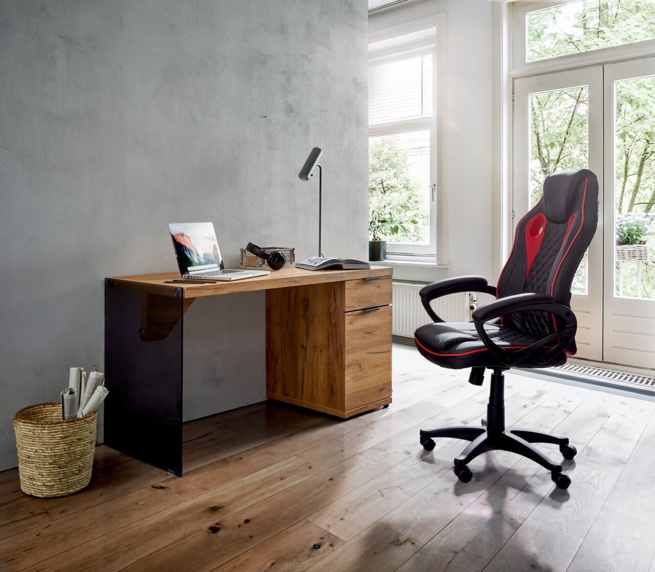 Moderner Gaming-Stuhl in Schwarz und Rot, seitliche Perspektive, neben einem Schreibtisch in einem hellen Raum mit großen Fenstern.