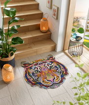 Bunte Fußmatte in Form eines Tigerkopfes mit abstraktem, geometrischem Design, platziert auf einem hellen Fliesenboden neben einer Holztreppe. Perspektive von oben.
