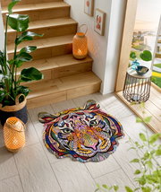 Bunte Fußmatte in Form eines Tigerkopfes mit abstraktem, geometrischem Design, platziert auf einem hellen Fliesenboden neben einer Holztreppe. Perspektive von oben.