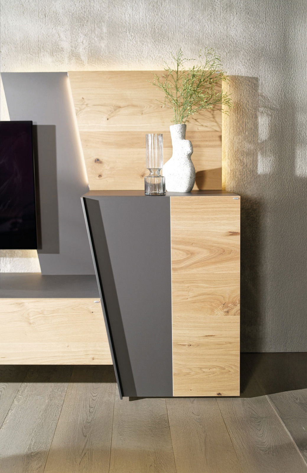 Moderne Wohnwand mit Holz- und Grauelementen, seitliche Perspektive, dekoriert mit einer Vase und einem Glas.