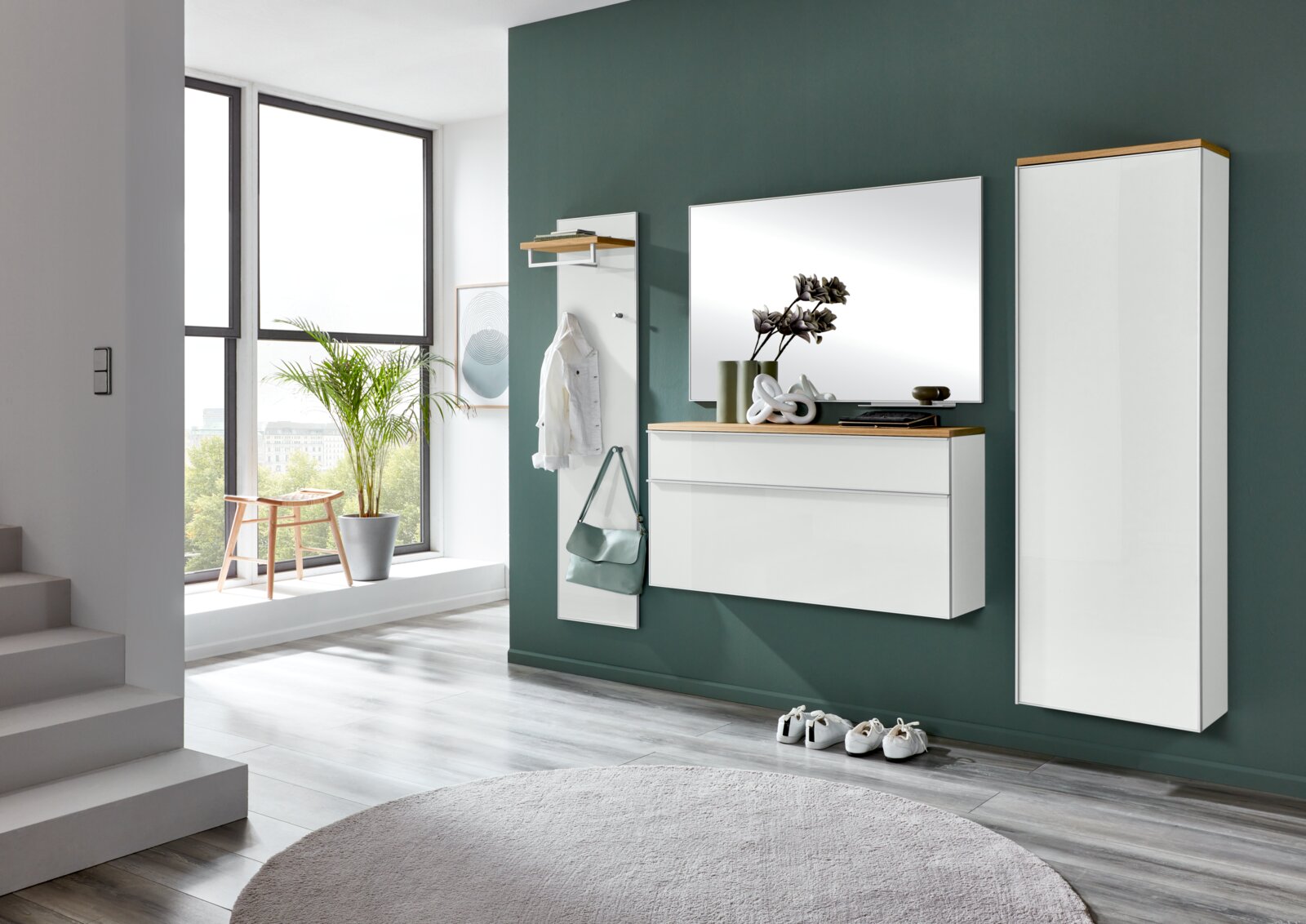 Modernes, wandmontiertes Flurmöbel-Set in Weiß mit Holzablagen, bestehend aus Garderobenpaneel mit Haken, Spiegel und Schuhschrank sowie hohem Schrank, gezeigt in frontaler Perspektive leicht von links in einem hellen Eingangsbereich.