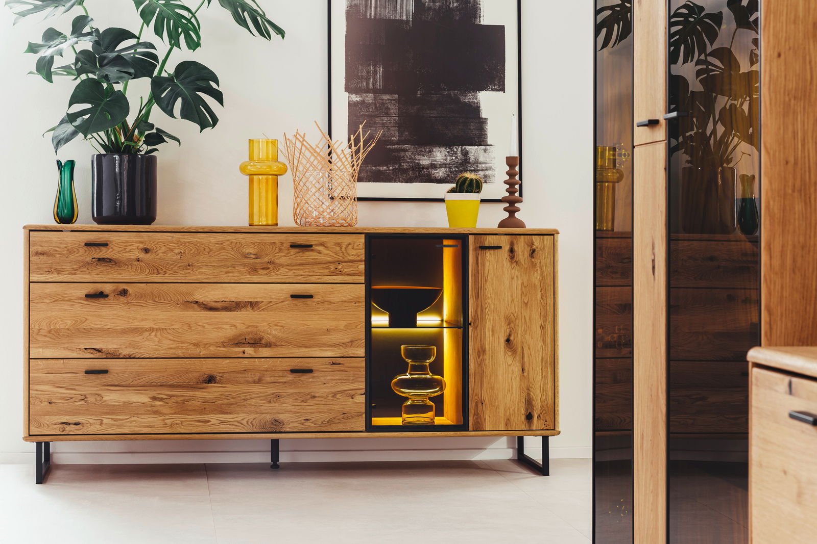 Holz-Sideboard mit Schubladen und Glastür, dekoriert mit Pflanzen und Vasen, aus frontaler Perspektive.