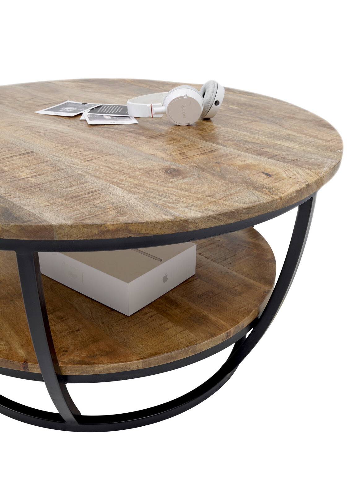 Runder Couchtisch aus Holz mit schwarzem Metallrahmen, von schräg oben fotografiert. Auf der Tischplatte liegen Kopfhörer und Fotos, darunter befindet sich ein Regal mit einer Box.
